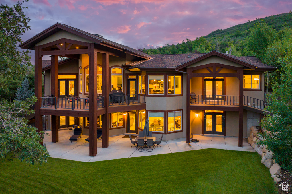 Back house at dusk featuring a patio, a balcony, a lawn, and a mountain view