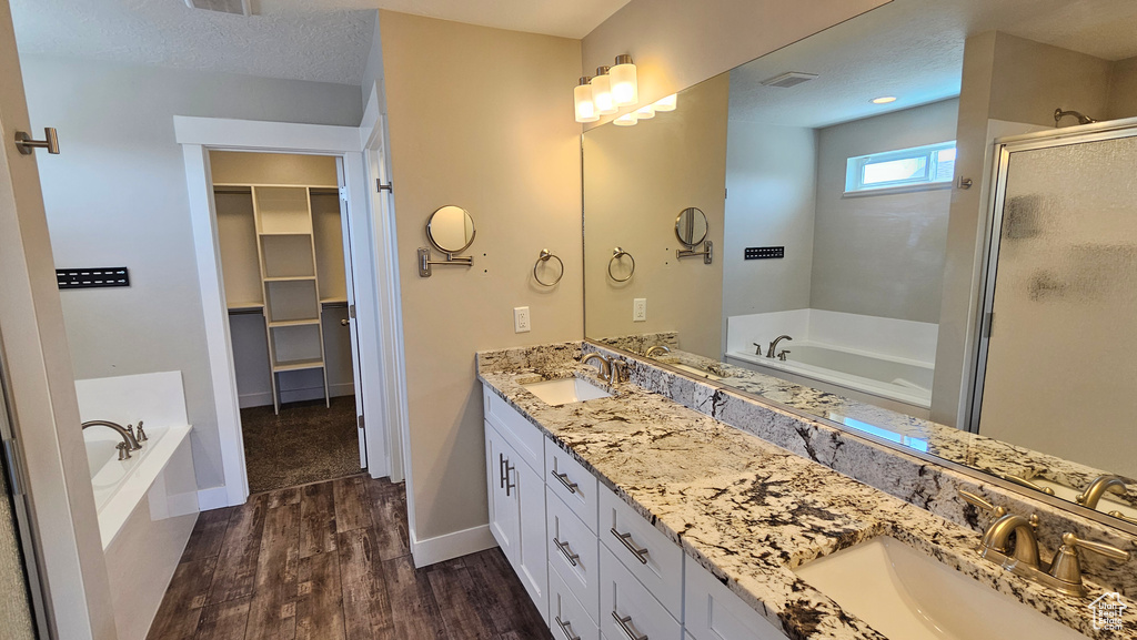 Bathroom featuring independent shower and bath, a textured ceiling, wood-type flooring, and double sink vanity