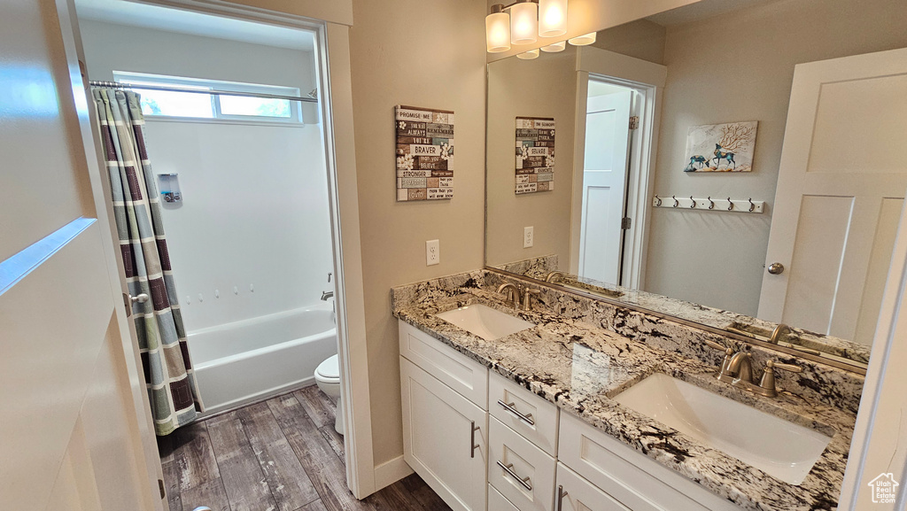 Full bathroom with double vanity, shower / bath combo, hardwood / wood-style floors, and toilet