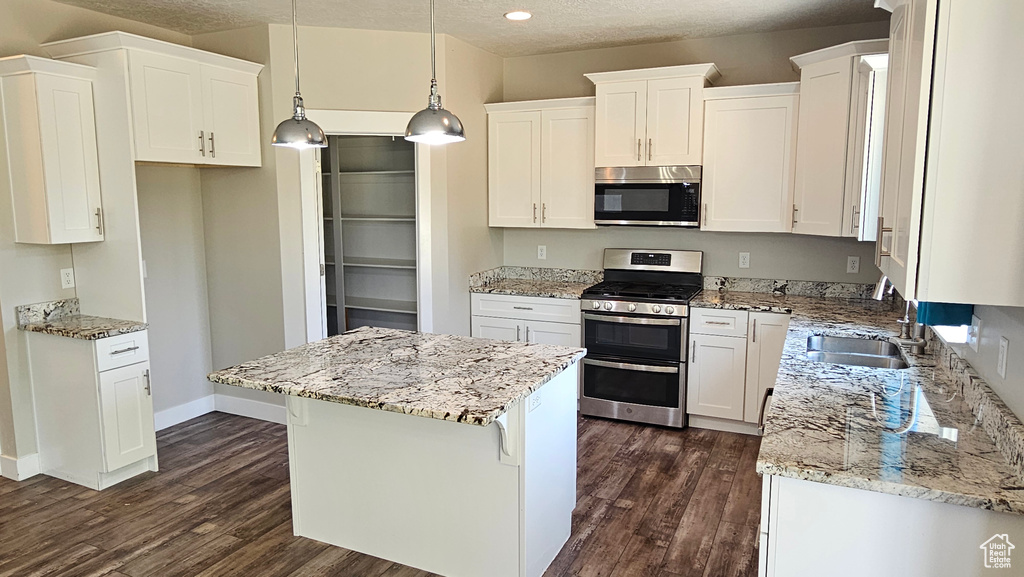 Kitchen with dark wood-type flooring, white cabinetry, a kitchen island, and stainless steel appliances