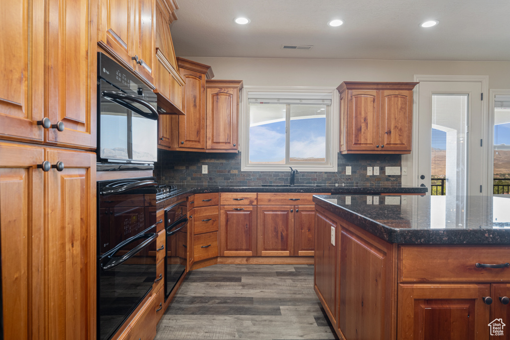 Kitchen with black double oven, a center island, backsplash, and dark wood-type flooring