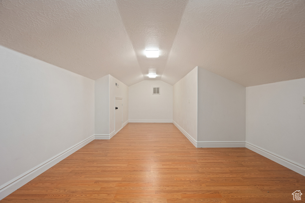 Bonus room with lofted ceiling, light hardwood / wood-style floors, and a textured ceiling