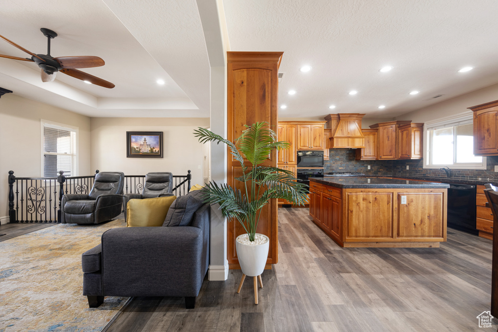 Kitchen featuring backsplash, premium range hood, hardwood / wood-style floors, and black appliances