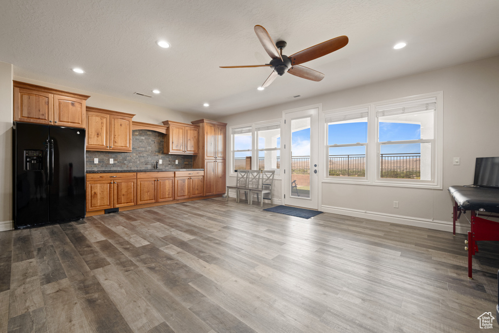 Kitchen featuring dark stone counters, black fridge, decorative backsplash, ceiling fan, and wood-type flooring