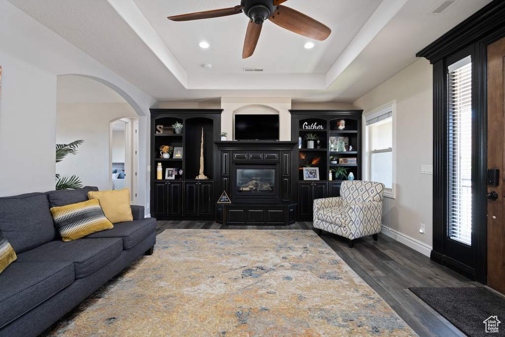 Living room featuring wood-type flooring, a healthy amount of sunlight, ceiling fan, and a raised ceiling