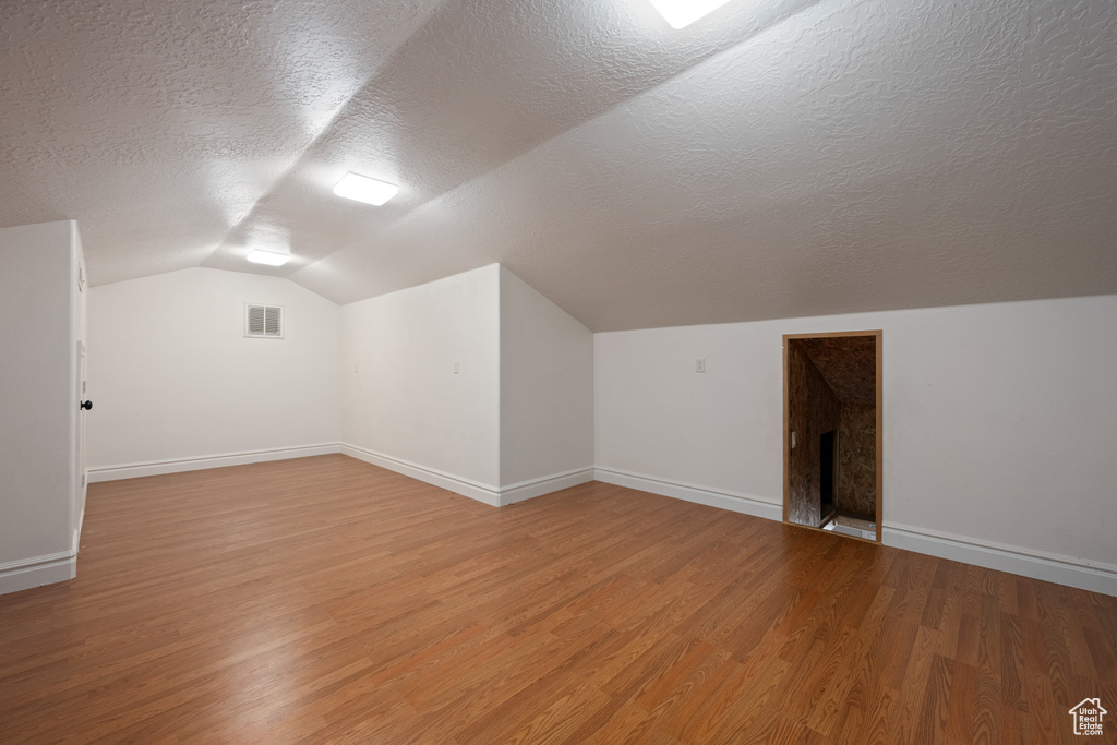 Additional living space featuring light hardwood / wood-style floors, a textured ceiling, and vaulted ceiling