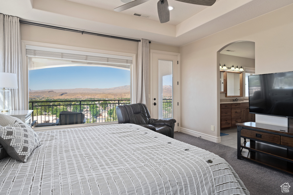 Bedroom with ceiling fan, a tray ceiling, ensuite bath, access to outside, and carpet