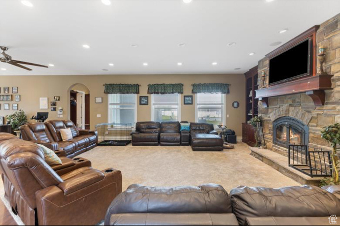 Carpeted living room with ceiling fan and a stone fireplace