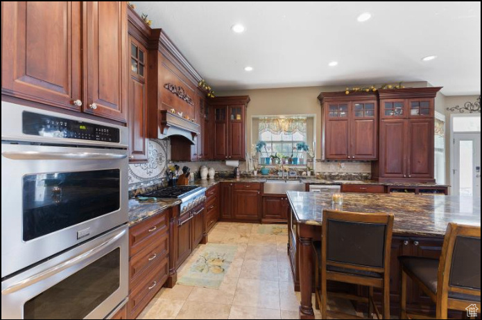 Kitchen featuring appliances with stainless steel finishes, dark stone countertops, light tile patterned floors, tasteful backsplash, and sink