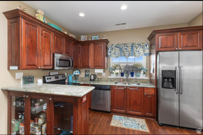 Kitchen featuring appliances with stainless steel finishes, light stone countertops, sink, dark hardwood / wood-style floors, and kitchen peninsula