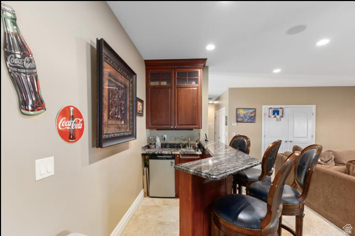 Kitchen with a breakfast bar, dark stone countertops, white dishwasher, light tile patterned floors, and kitchen peninsula