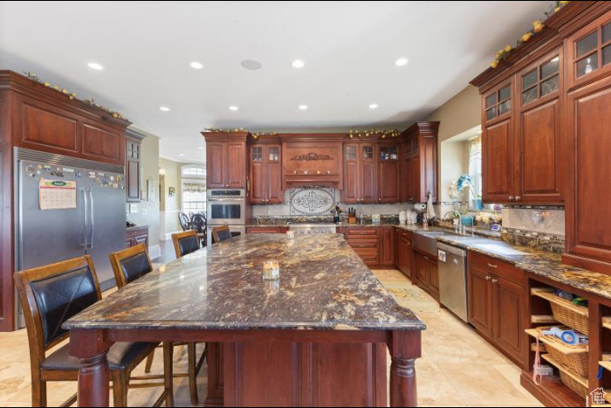 Kitchen featuring decorative backsplash, dark stone counters, light tile patterned floors, a center island, and stainless steel appliances