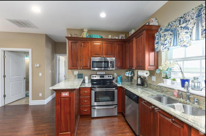 Kitchen with appliances with stainless steel finishes, dark hardwood / wood-style floors, sink, and light stone countertops