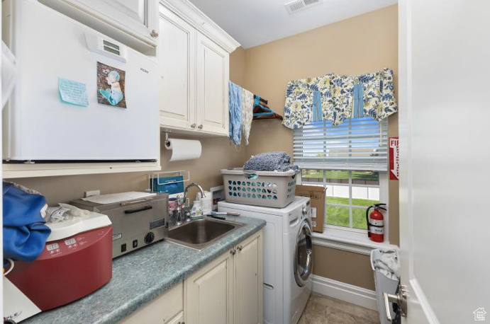 Clothes washing area with sink, washer / clothes dryer, light tile patterned floors, and cabinets