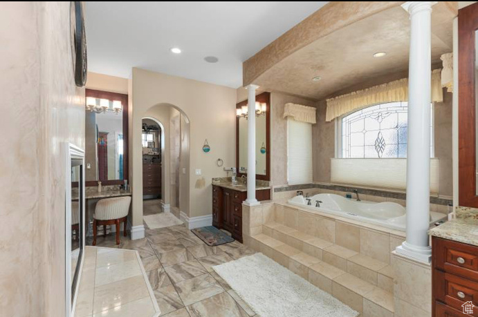 Bathroom with tiled tub, tile patterned floors, vanity, and decorative columns