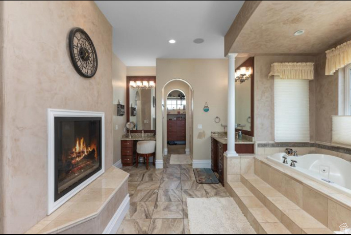 Bathroom with a fireplace, ornate columns, tile patterned flooring, a relaxing tiled tub, and vanity