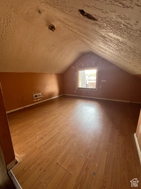 Bonus room with a textured ceiling, hardwood / wood-style flooring, and vaulted ceiling