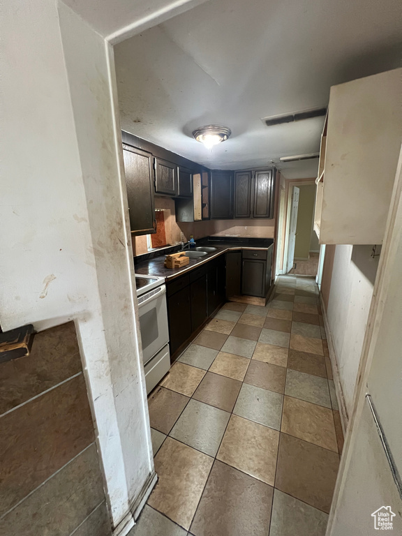 Kitchen with dark brown cabinetry, sink, electric range, and light tile patterned floors