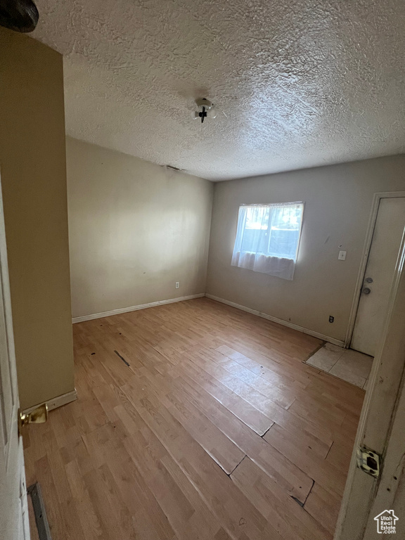 Empty room with light hardwood / wood-style flooring and a textured ceiling