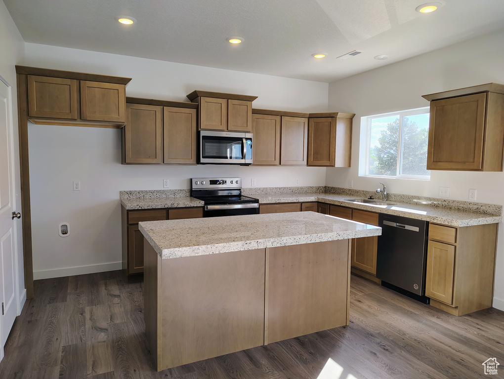 Kitchen with sink, stainless steel appliances, dark hardwood / wood-style floors, a center island, and light stone countertops