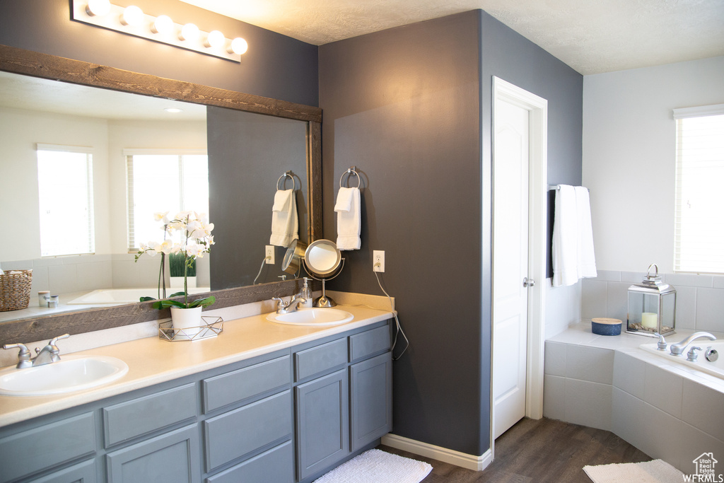 Bathroom featuring plenty of natural light, double vanity, tiled tub, and hardwood / wood-style flooring