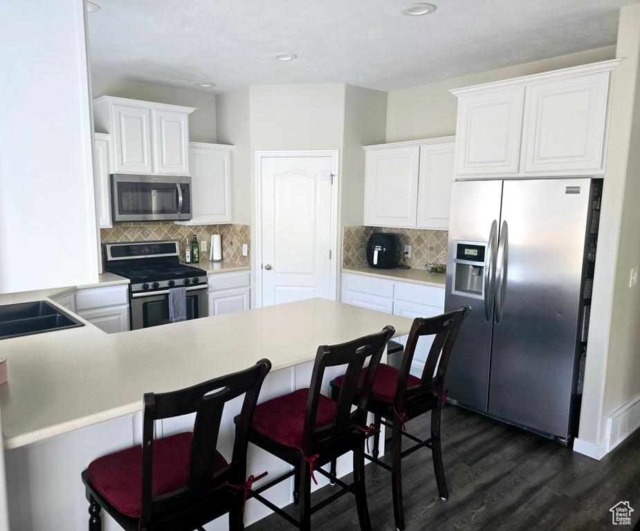 Kitchen featuring appliances with stainless steel finishes, dark wood-type flooring, white cabinets, and backsplash