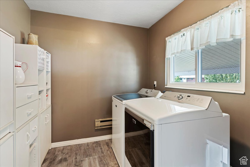 Laundry room with separate washer and dryer, cabinets, and hardwood / wood-style flooring