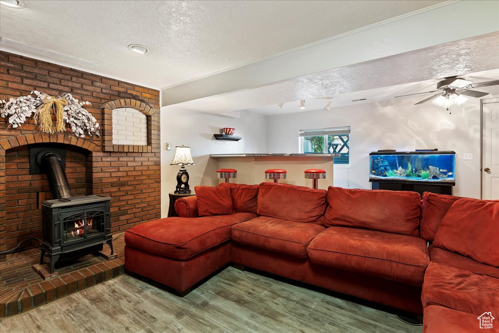 Living room with ceiling fan, a wood stove, hardwood / wood-style floors, and a textured ceiling