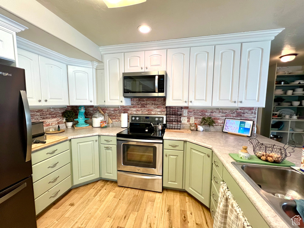 Kitchen with light hardwood / wood-style flooring, green cabinetry, white cabinets, and stainless steel appliances