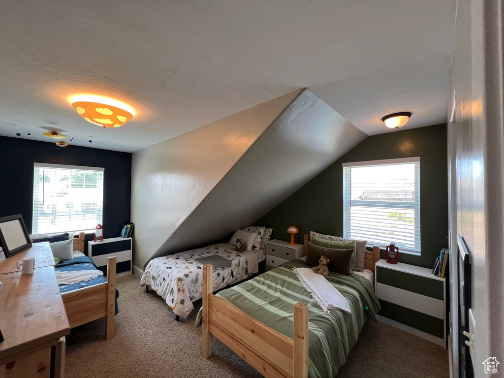 Carpeted bedroom with a textured ceiling, multiple windows, and lofted ceiling