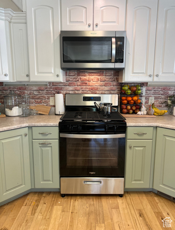 Kitchen with decorative backsplash, white cabinets, appliances with stainless steel finishes, and light wood-type flooring