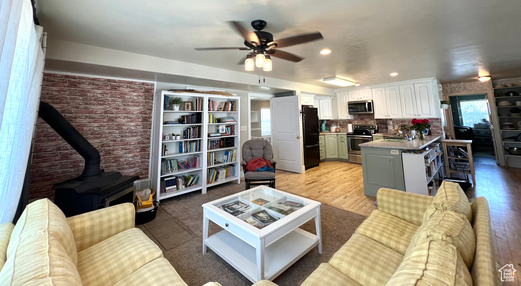 Living room with brick wall, a wood stove, ceiling fan, and light hardwood / wood-style floors