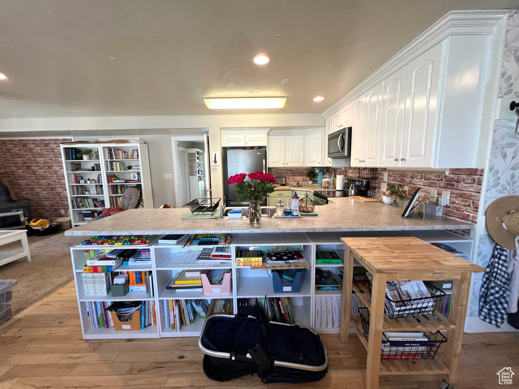 Kitchen with appliances with stainless steel finishes, light wood-type flooring, kitchen peninsula, and white cabinets