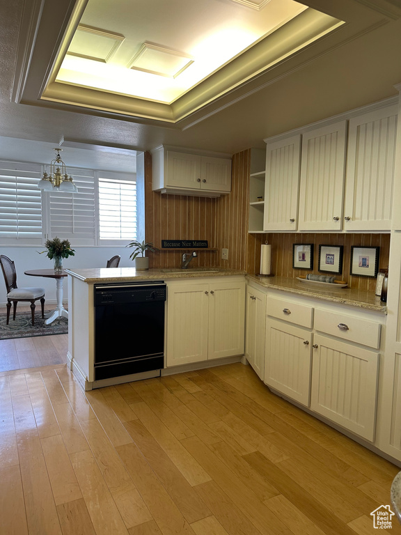 Kitchen with black dishwasher, sink, light wood-type flooring, a raised ceiling, and a notable chandelier