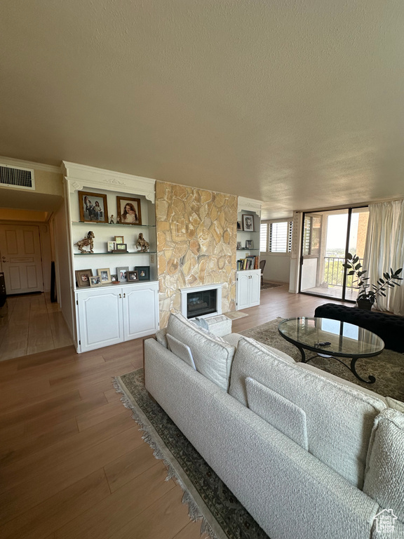 Living room featuring built in features, light hardwood / wood-style flooring, a textured ceiling, and a stone fireplace