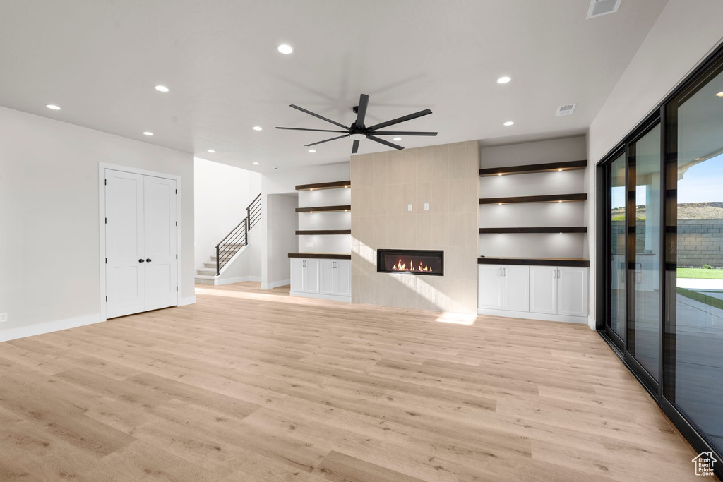 Unfurnished living room featuring ceiling fan, light wood-type flooring, and a tile fireplace