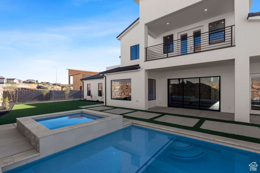 Back of house with a balcony, a patio, a yard, and an in ground hot tub