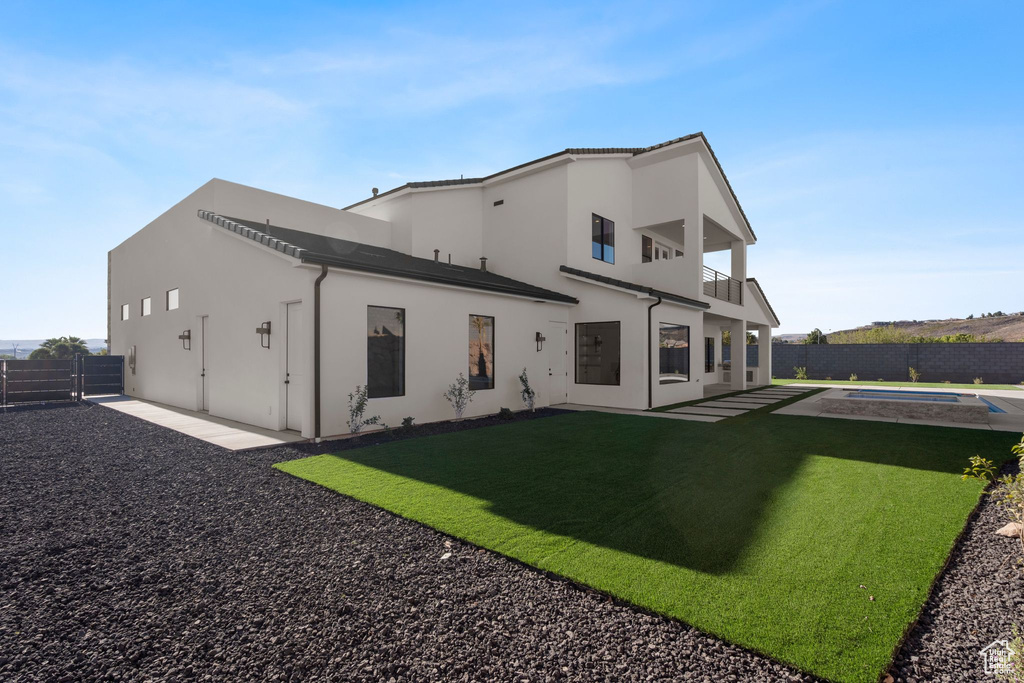 Back of property featuring a balcony, a patio, a fenced in pool, and a yard