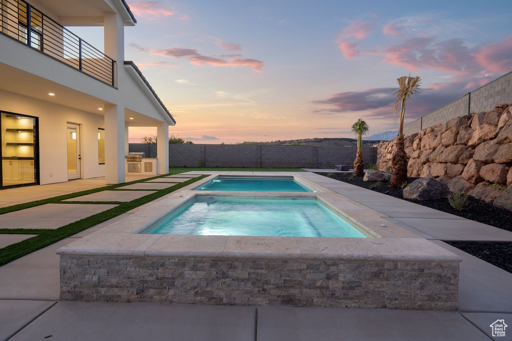 Pool at dusk featuring an in ground hot tub and a patio area