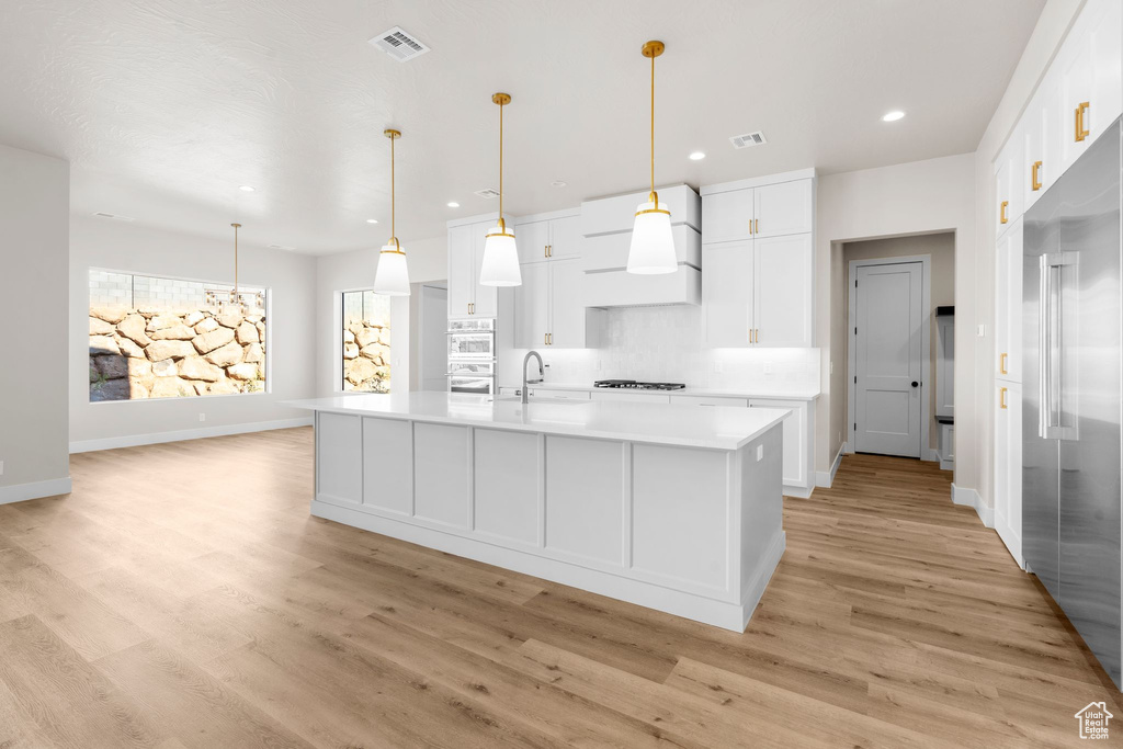 Kitchen with a kitchen island with sink, light hardwood / wood-style flooring, hanging light fixtures, and white cabinetry