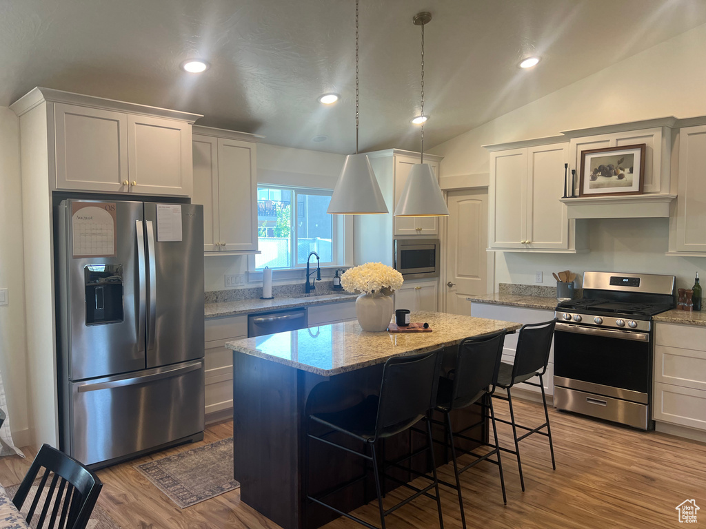 Kitchen featuring a center island, wood-type flooring, stainless steel appliances, and vaulted ceiling