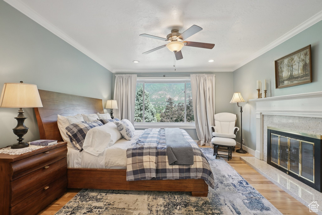 Bedroom featuring light wood-type flooring, crown molding, a high end fireplace, and ceiling fan