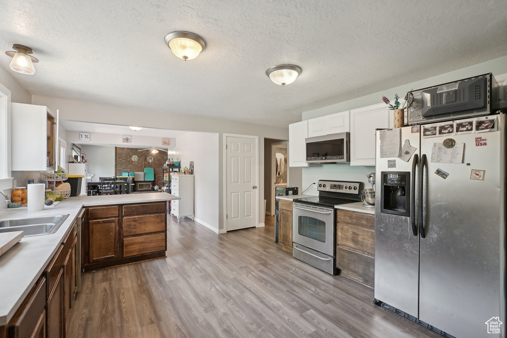 Kitchen featuring stainless steel appliances, white cabinets, sink, light hardwood / wood-style floors, and a textured ceiling