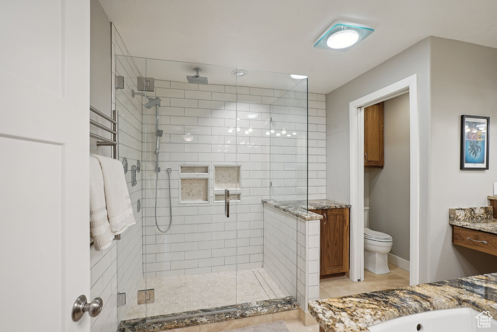 Bathroom with a shower with shower door, vanity, tile patterned flooring, and toilet