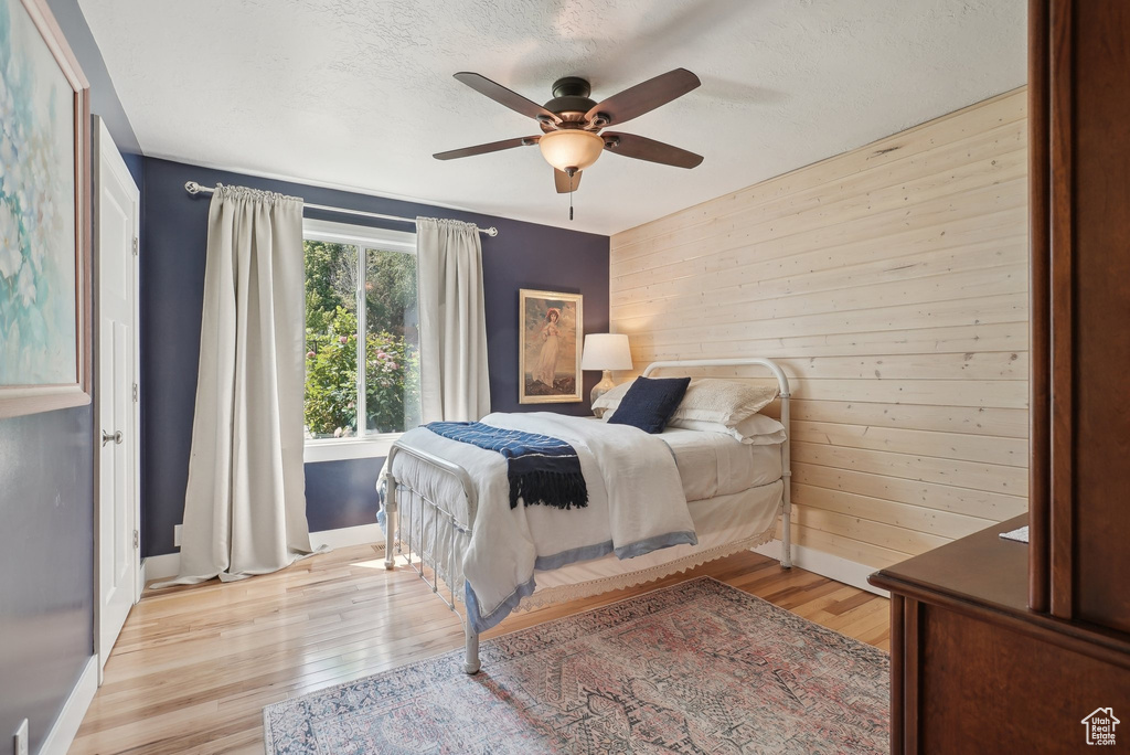 Bedroom with light hardwood / wood-style floors, wood walls, and ceiling fan