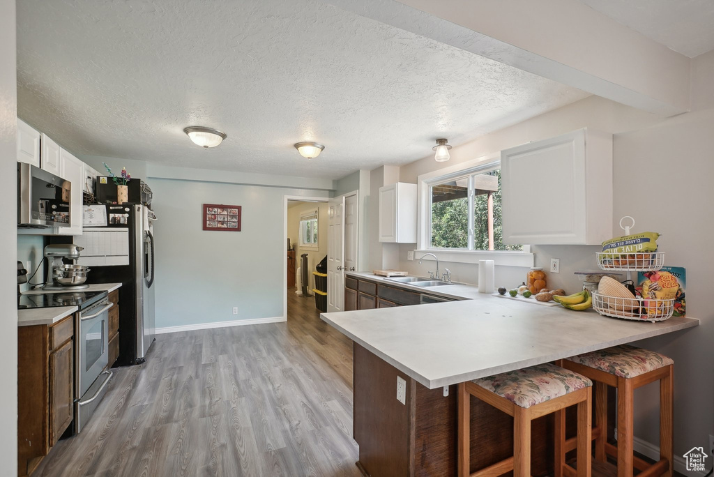 Kitchen featuring appliances with stainless steel finishes, sink, light wood-type flooring, a textured ceiling, and white cabinetry