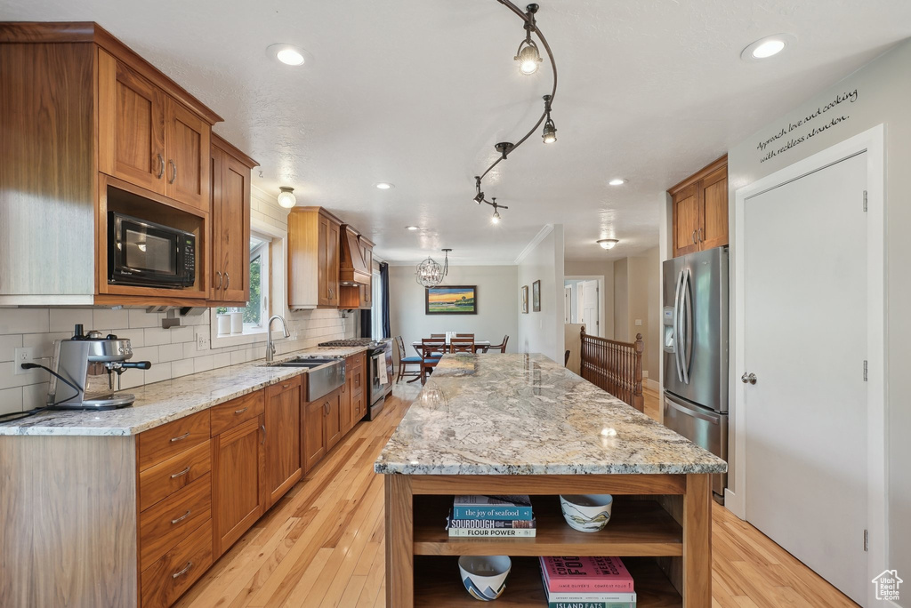 Kitchen with light wood-type flooring, a center island, appliances with stainless steel finishes, and light stone countertops