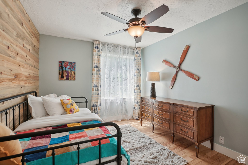 Bedroom with wooden walls, light wood-type flooring, ceiling fan, and a textured ceiling