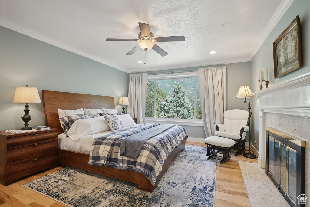 Bedroom featuring a fireplace, light hardwood / wood-style flooring, ornamental molding, and ceiling fan