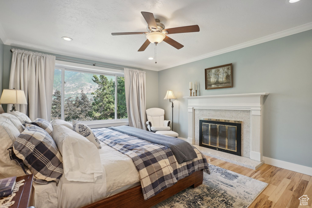 Bedroom with a high end fireplace, light wood-type flooring, ceiling fan, and ornamental molding